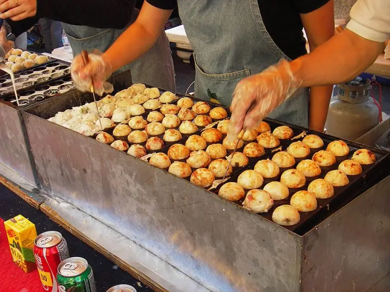 Takoyaki vendido como comida rápida no Japão Porção de takoyaki com molho e coberturas em bandeja