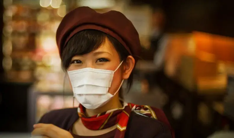 Une jeune femme avec un masque vert clair assise dans un wagon de métro tokyoïte typique
