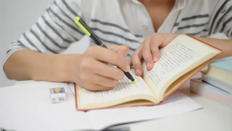 Mulher concentrada estudando com livros abertos em uma mesa de madeira