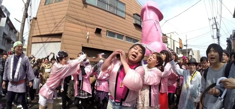 Teilnehmerinnen und Teilnehmer tragen beim Kanamara Matsuri in Kawasaki eine mikoshi mit einer grossen Phallus-Form durch die Strassen; festliche Stimmung mit vielen Besuchern
