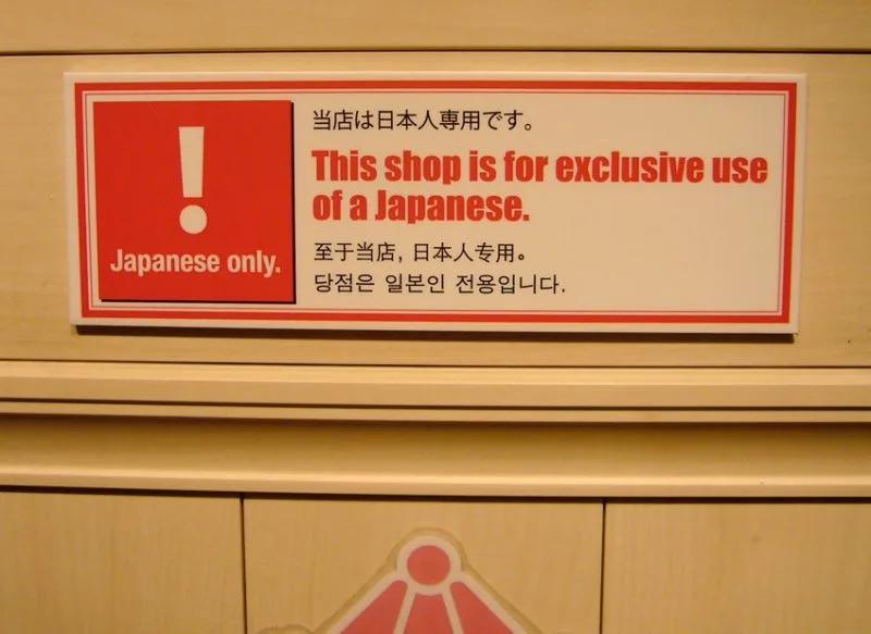 Estabelecimentos que proíbem entrada de estrangeiros Placa de um estabelecimento escrita em japonês, inglês, chinês e coreano. A placa avisa que a loja é uso de exclusivo de japoneses.