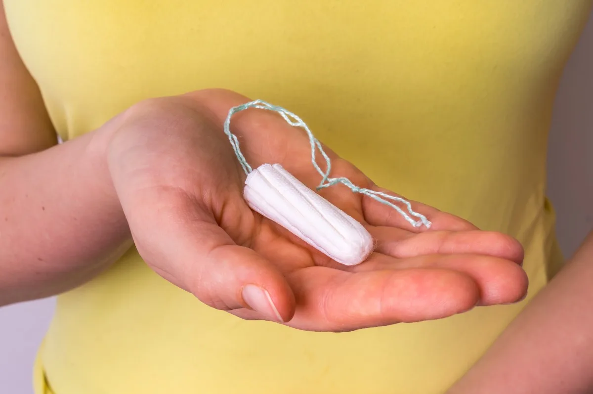 Young woman holding menstruation tampon in hand