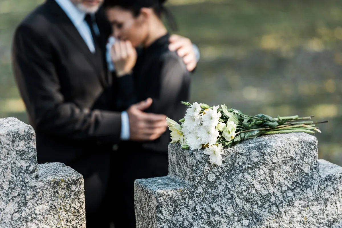 selective focus of bouquet on tombstone near man hugging woman